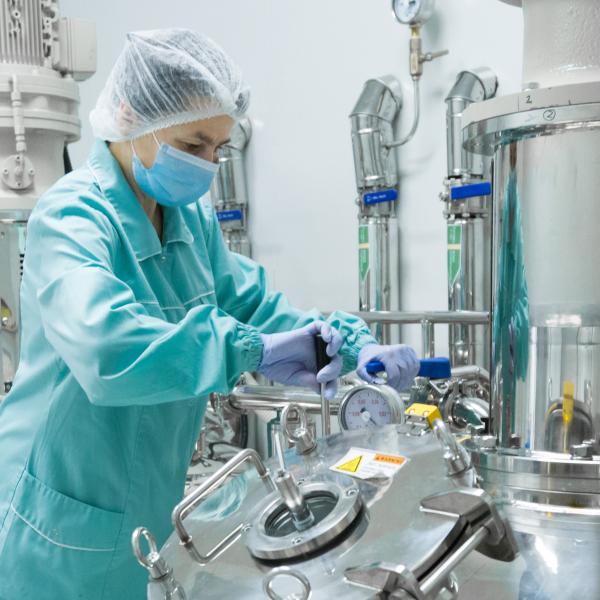 Pharmaceutical factory woman worker in protective clothing operating production line in sterile environment