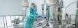 Pharmaceutical factory woman worker in protective clothing operating production line in sterile environment